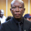Close-up of an African man in a black suit and tie at a formal event, with a blurred crowd in the background