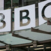 Front of a building with large white signs displaying the letters BBC on glass panels.