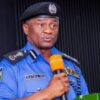 Police officer in a blue uniform speaks into an orange microphone at a podium during a formal event.