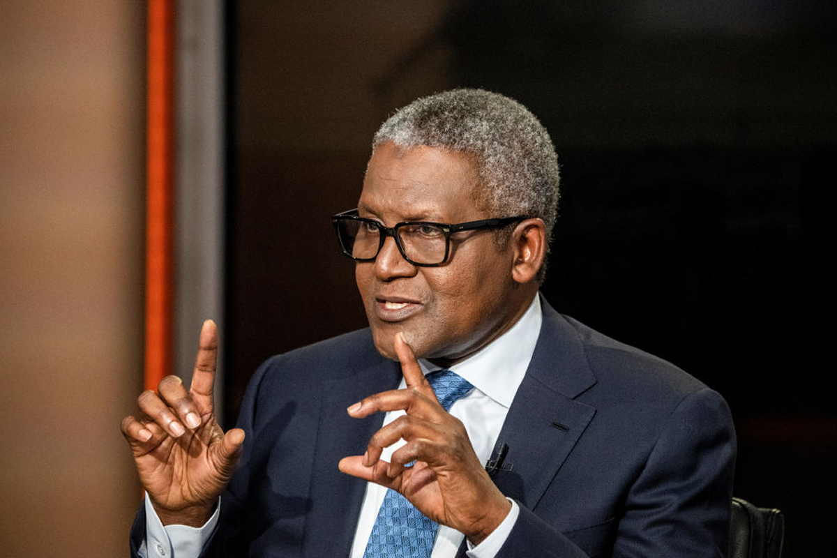 Man in a dark suit and blue tie speaks, using hand gestures while seated or standing off-camera.