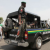 Police officers in tactical gear on a black pickup with an open back patrolling a street.