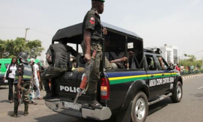Police officers in tactical gear on a black pickup with an open back patrolling a street.