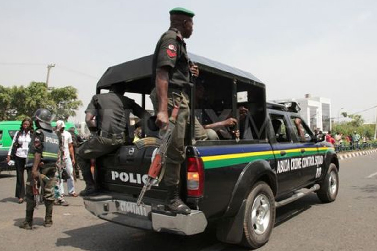 Police officers in tactical gear on a black pickup with an open back patrolling a street.
