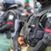 Armored police officer in tactical vest and helmet, holding a rifle.