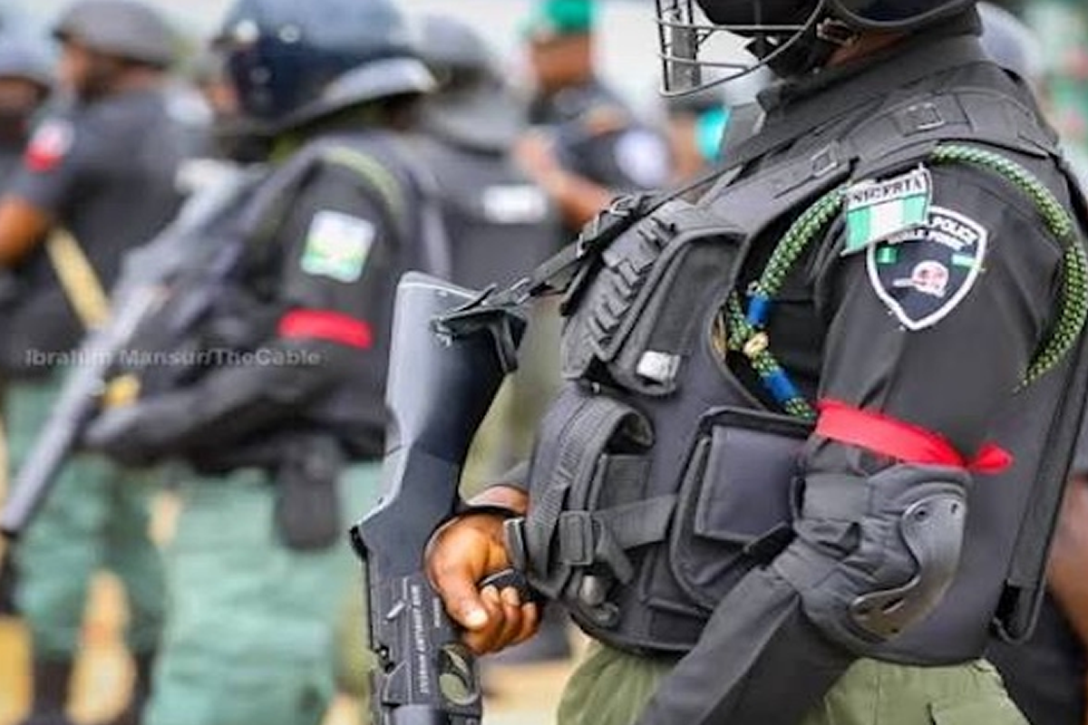 Armored police officer in tactical vest and helmet, holding a rifle.