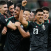 Mexican national team players celebrate together on the field, embracing in black jerseys with green trim and the number 23 visible on one player's chest.