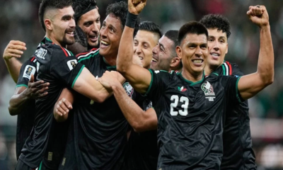 Mexican national team players celebrate together on the field, embracing in black jerseys with green trim and the number 23 visible on one player's chest.