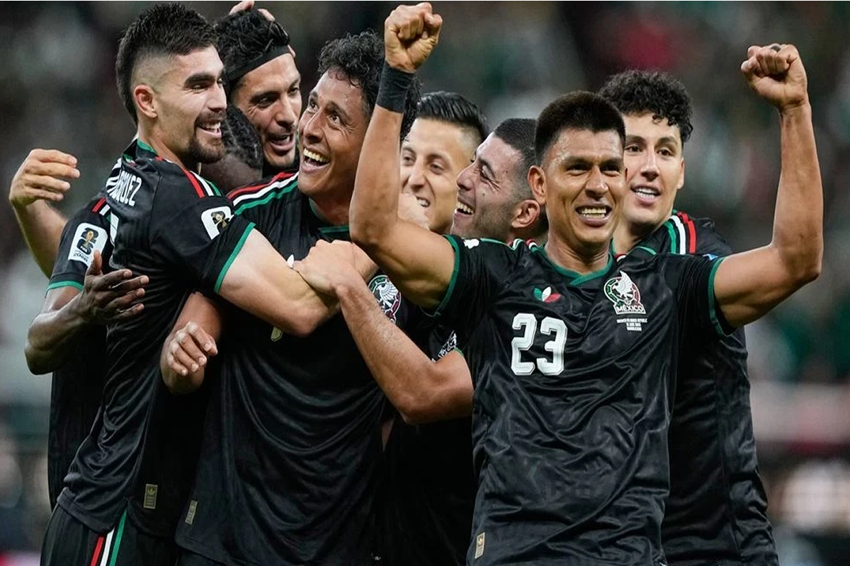 Mexican national team players celebrate together on the field, embracing in black jerseys with green trim and the number 23 visible on one player's chest.