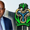 Man in a blue suit stands next to the Central Bank of Nigeria logo on a tall building in the background.
