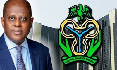 Man in a blue suit stands next to the Central Bank of Nigeria logo on a tall building in the background.