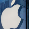 Large white Apple logo mounted on a blue-tinted glass building façade.