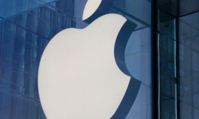 Large white Apple logo mounted on a blue-tinted glass building façade.