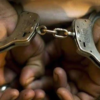 Close-up of hands in metal handcuffs being linked/unlinked, showing chain between cuffs from a close angle, bare fingers visible
