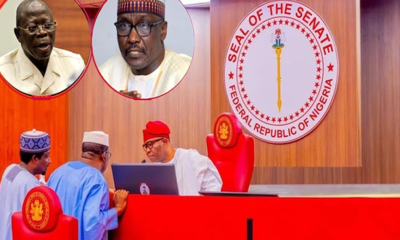 Senate chamber scene with the Seal of the Senate of Nigeria on the wall and three officials at a red desk discussing over a laptop.