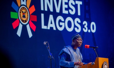 Man in blue traditional attire speaks at a podium during the 'Invest Lagos 3.0' event; Lagos state seal on the lectern and a large banner behind him.