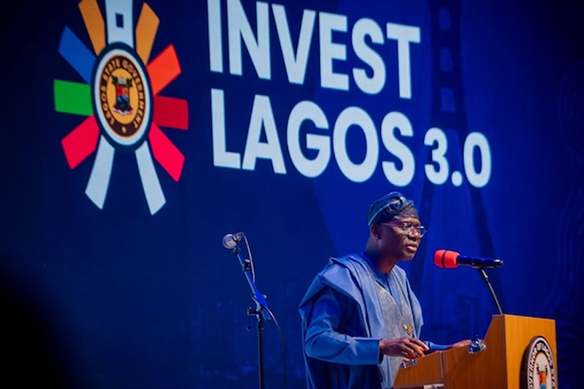 Man in blue traditional attire speaks at a podium during the 'Invest Lagos 3.0' event; Lagos state seal on the lectern and a large banner behind him.