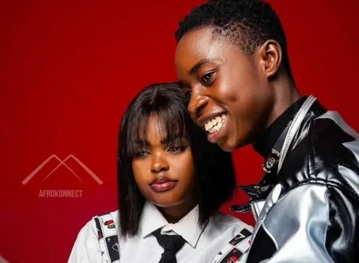 Two young people pose together against a red backdrop; woman wears a white shirt and tie, man in a shiny jacket, AFROKONNECT logo visible in the background.
