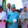 Dignitaries cut a green ribbon at a ceremonial event, with balloons and a banner in the background.