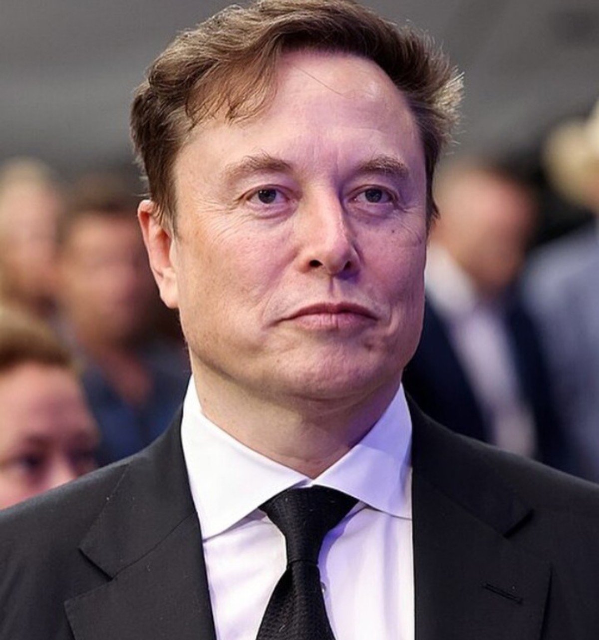 Man in a black suit and white shirt at a formal event, looking straight ahead.