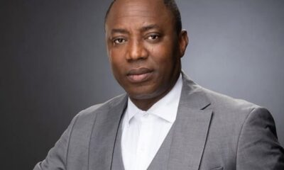 Professional headshot: man in a gray suit and white shirt against a dark studio background.