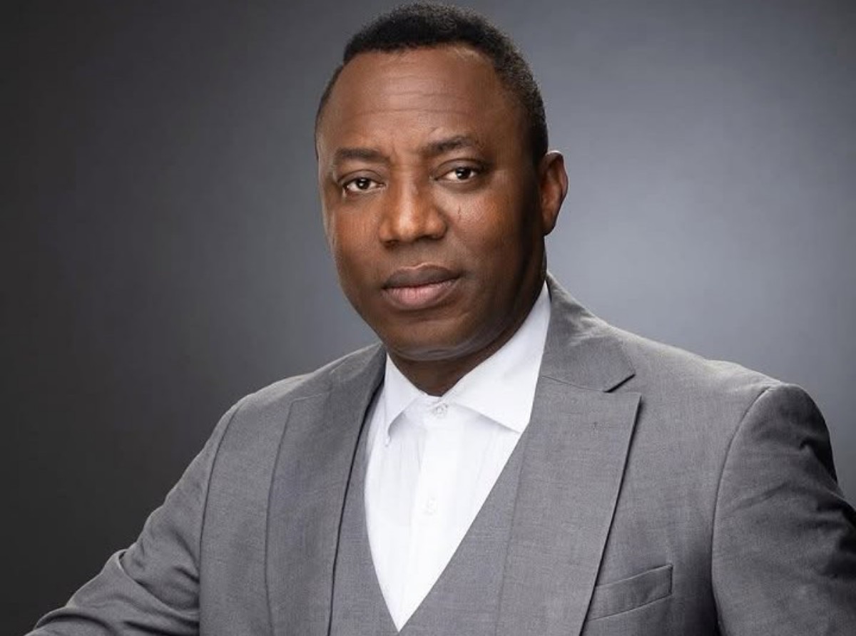 Professional headshot: man in a gray suit and white shirt against a dark studio background.