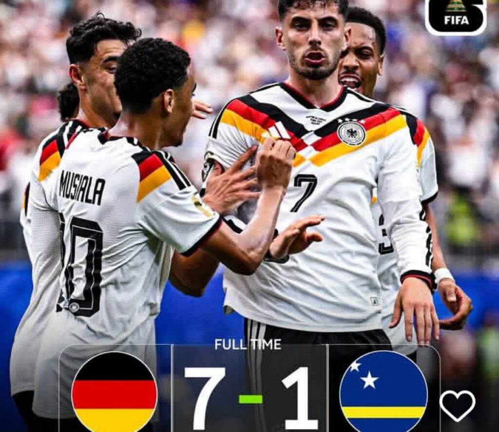 Germany players celebrate a 7–1 victory, with Musiala on the back of one jersey and the FIFA logo in the corner.