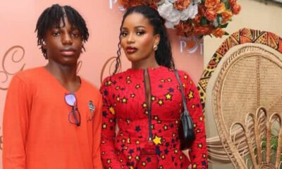 Two models posing at a fashion event: the woman in a red star-pattern dress with a black bag, and the man in an orange shirt against a pink backdrop.