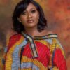 Portrait of a woman with shoulder-length black hair wearing a vibrant African print blouse against a warm mottled backdrop.