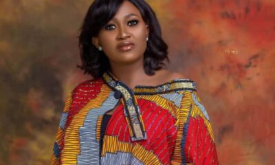 Portrait of a woman with shoulder-length black hair wearing a vibrant African print blouse against a warm mottled backdrop.