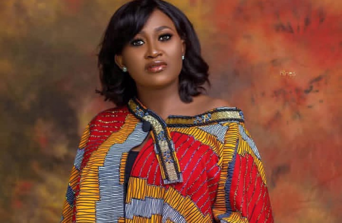 Portrait of a woman with shoulder-length black hair wearing a vibrant African print blouse against a warm mottled backdrop.