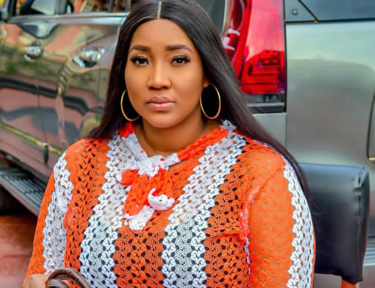 Woman with long black hair wearing an orange and white crochet top, standing in front of a parked SUV.