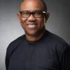 Smiling African American man wearing black-framed glasses and a dark top, against a gray studio backdrop.