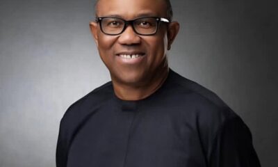 Smiling African American man wearing black-framed glasses and a dark top, against a gray studio backdrop.