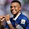 Soccer player in a blue striped jersey celebrating with fists clenched and a smile on his face.