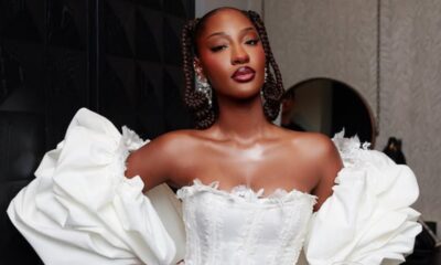 Woman wearing a white off-shoulder ball gown with voluminous sleeves and braided hairstyle, posing indoors.