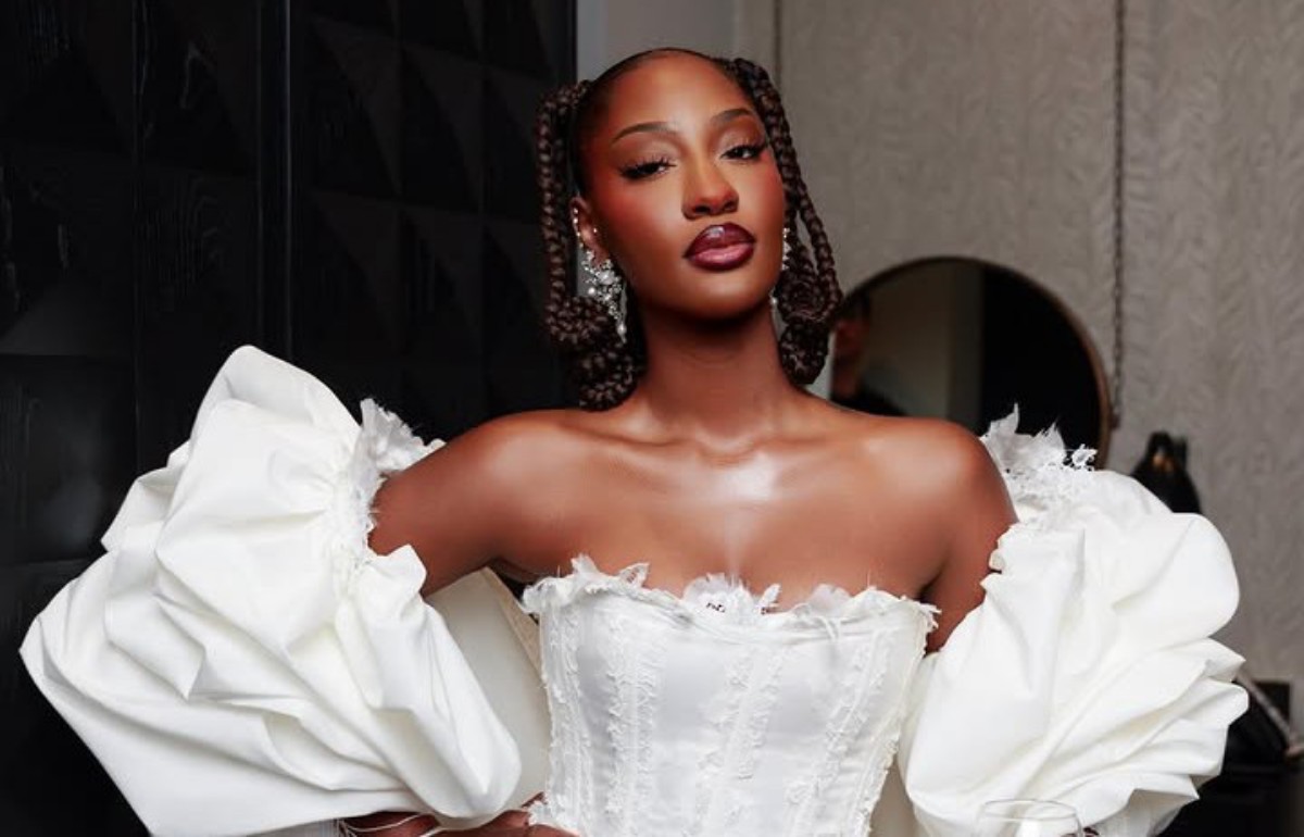 Woman wearing a white off-shoulder ball gown with voluminous sleeves and braided hairstyle, posing indoors.