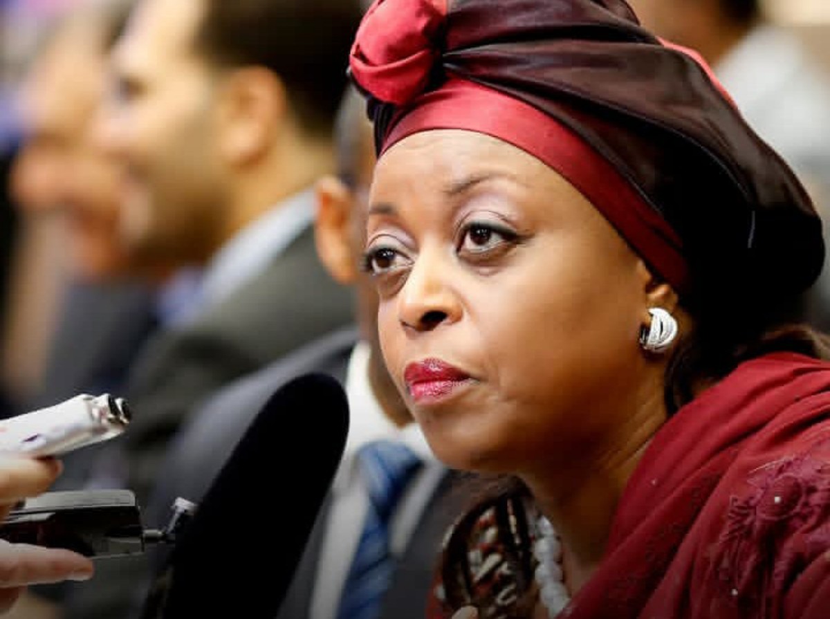 Woman in a red headwrap being interviewed, microphone held up to her lips at a press event