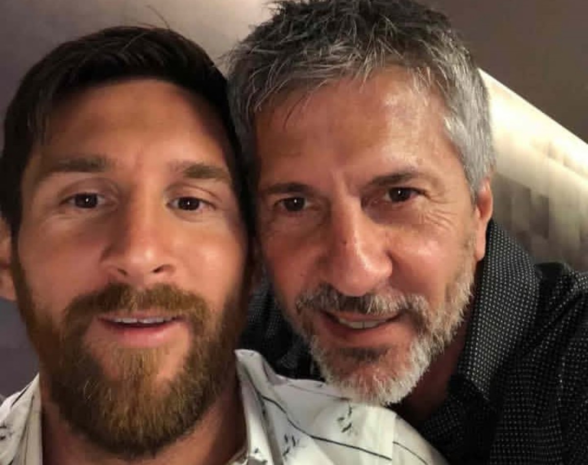 Two men close together taking a selfie, smiling at the camera in a casual setting with one man having a beard and the other gray hair.