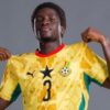 Soccer player wearing a yellow Ghana national team jersey with number 3, lifting the shirt collar in a posing shot.