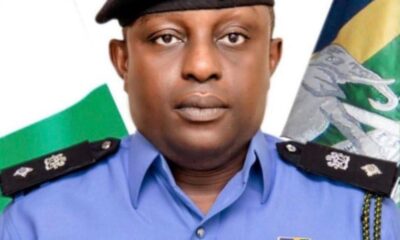 Portrait of a male police officer in a blue uniform with a beret, name tag reads INEDU A OKOKON, medals on his chest, flags in the background.