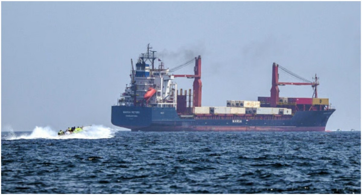 Large cargo ship on the open sea with a small speedboat ahead, suggesting a rescue or escort operation in progress.