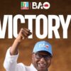 Smiling man in glasses and a light-blue cap raises a clenched fist with a large 'VICTORY!' headline behind him; APC and BAO logos appear at the top, suggesting a celebration poster.