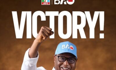 Smiling man in glasses and a light-blue cap raises a clenched fist with a large 'VICTORY!' headline behind him; APC and BAO logos appear at the top, suggesting a celebration poster.