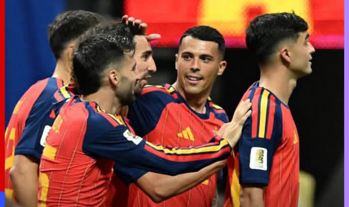Spanish soccer players in red-blue jerseys celebrate a goal, arms around each other in a group hug on the field
