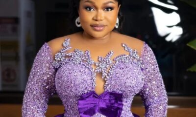 Woman in a lavender, beaded gown with a large purple bow, posing for a photo with a soft smile and elegant jewelry.