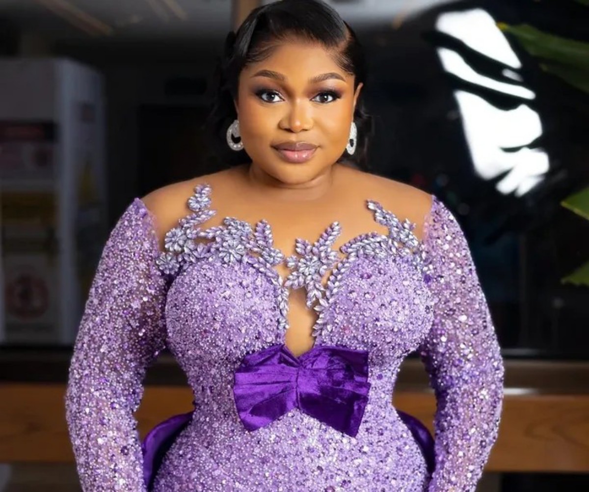 Woman in a lavender, beaded gown with a large purple bow, posing for a photo with a soft smile and elegant jewelry.