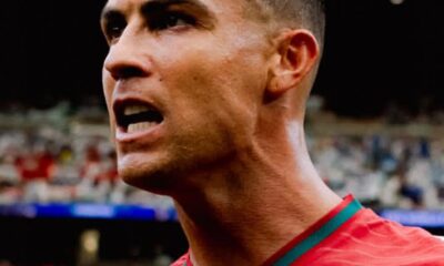 Close-up of a male soccer player shouting on the field, wearing a red jersey with green trim.