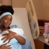 Mother in a hospital bed gently cradling her newborn swaddled in a white blanket.