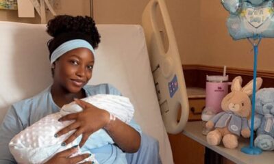 Mother in a hospital bed gently cradling her newborn swaddled in a white blanket.