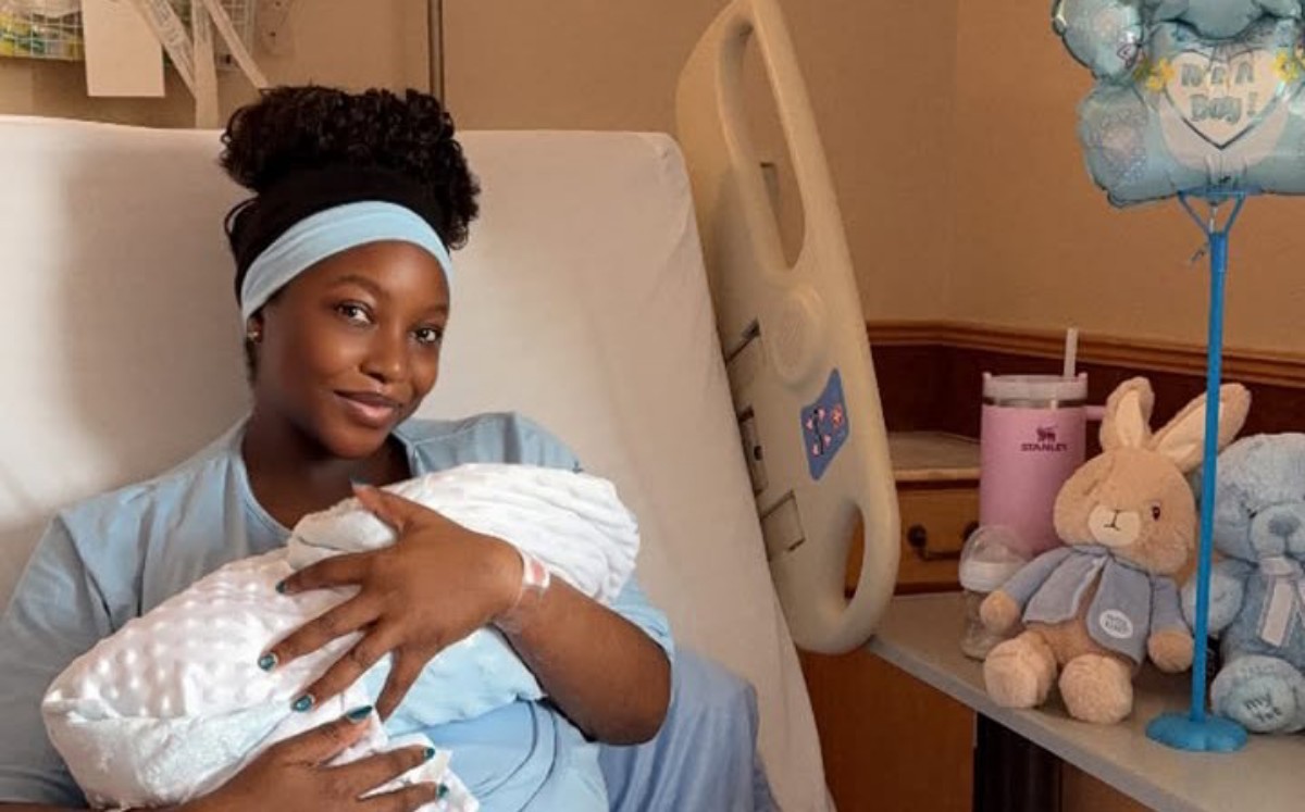 Mother in a hospital bed gently cradling her newborn swaddled in a white blanket.